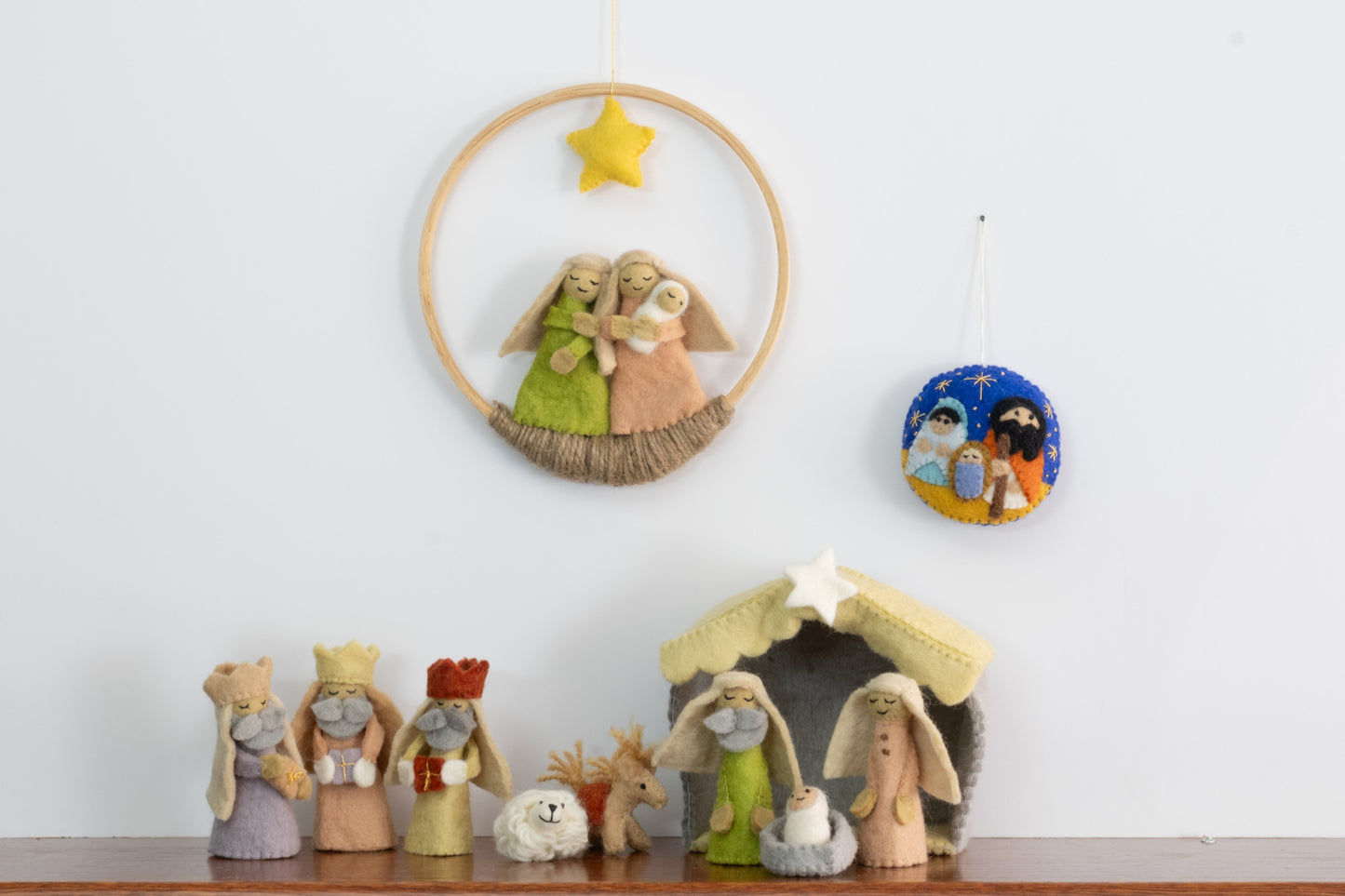 Felt ornament in a circle shape showing the nativity scene of Mary, Joseph, and baby Jesus underneath the night sky behind a full nativity scene set.