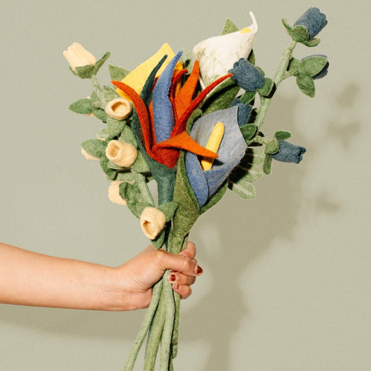 Hand holding out a bunch of felt Bird of Paradise flowers in orange, blue, and white with other felt flowers.