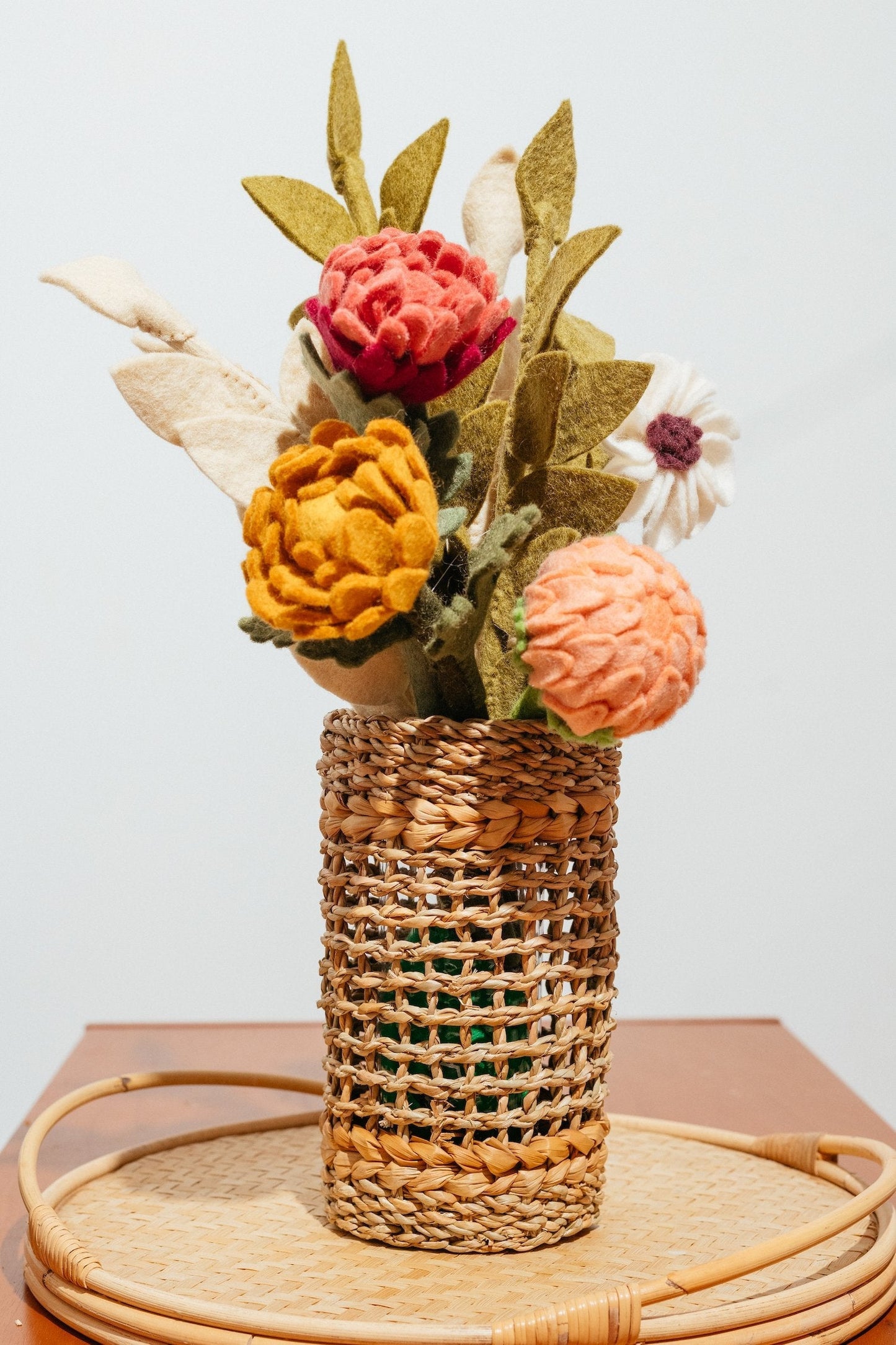 Closeup of tall brown woven vase with glass insert and felt flowers on brown table..