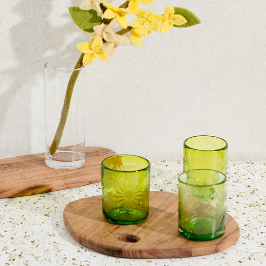 Brown wood round cutting board with green glasses. Additional board in background.