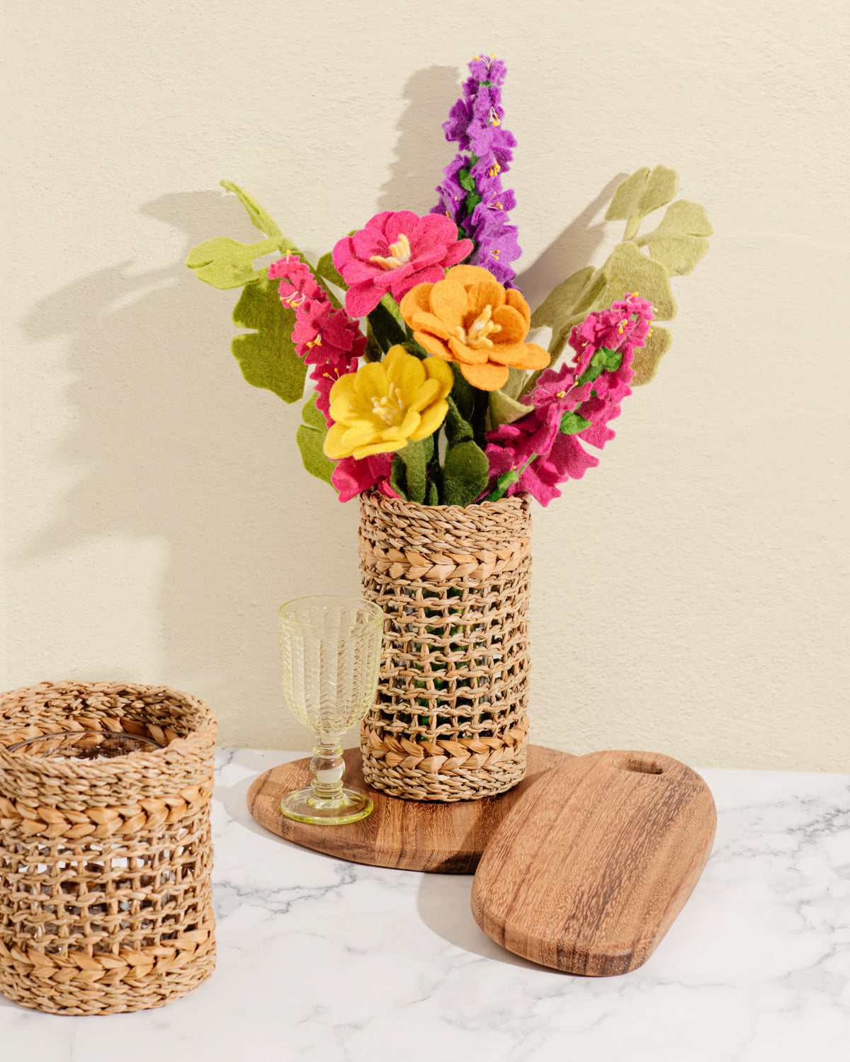Pink, orange and yellow felt Camellia flowers in brown woven vase with other various felt flowers.