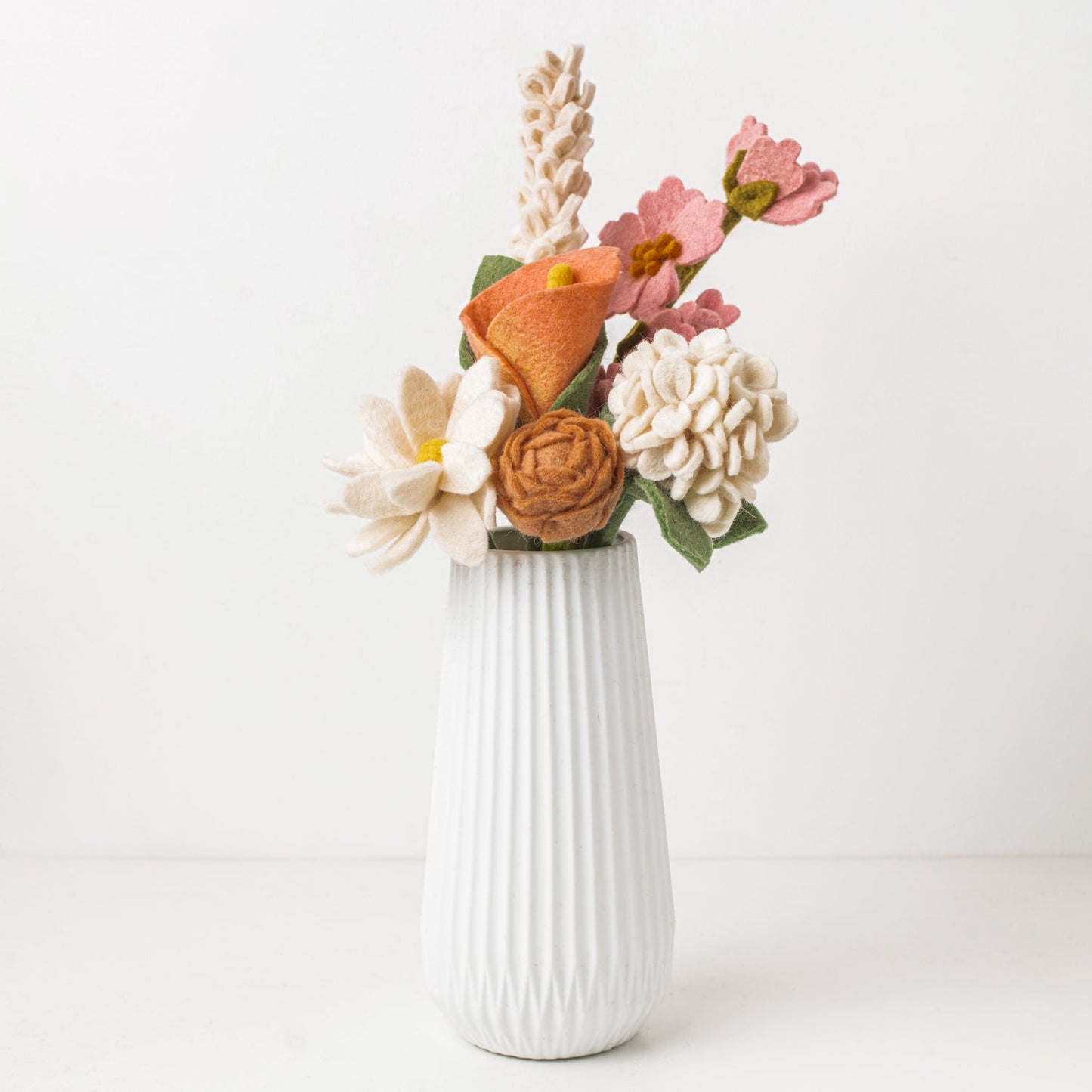 Pink, white and green felt floral arrangement in a white vase.