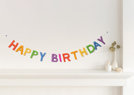 Felt garland spelling Happy Birthday in bright classic rainbow colors hung over mantel.