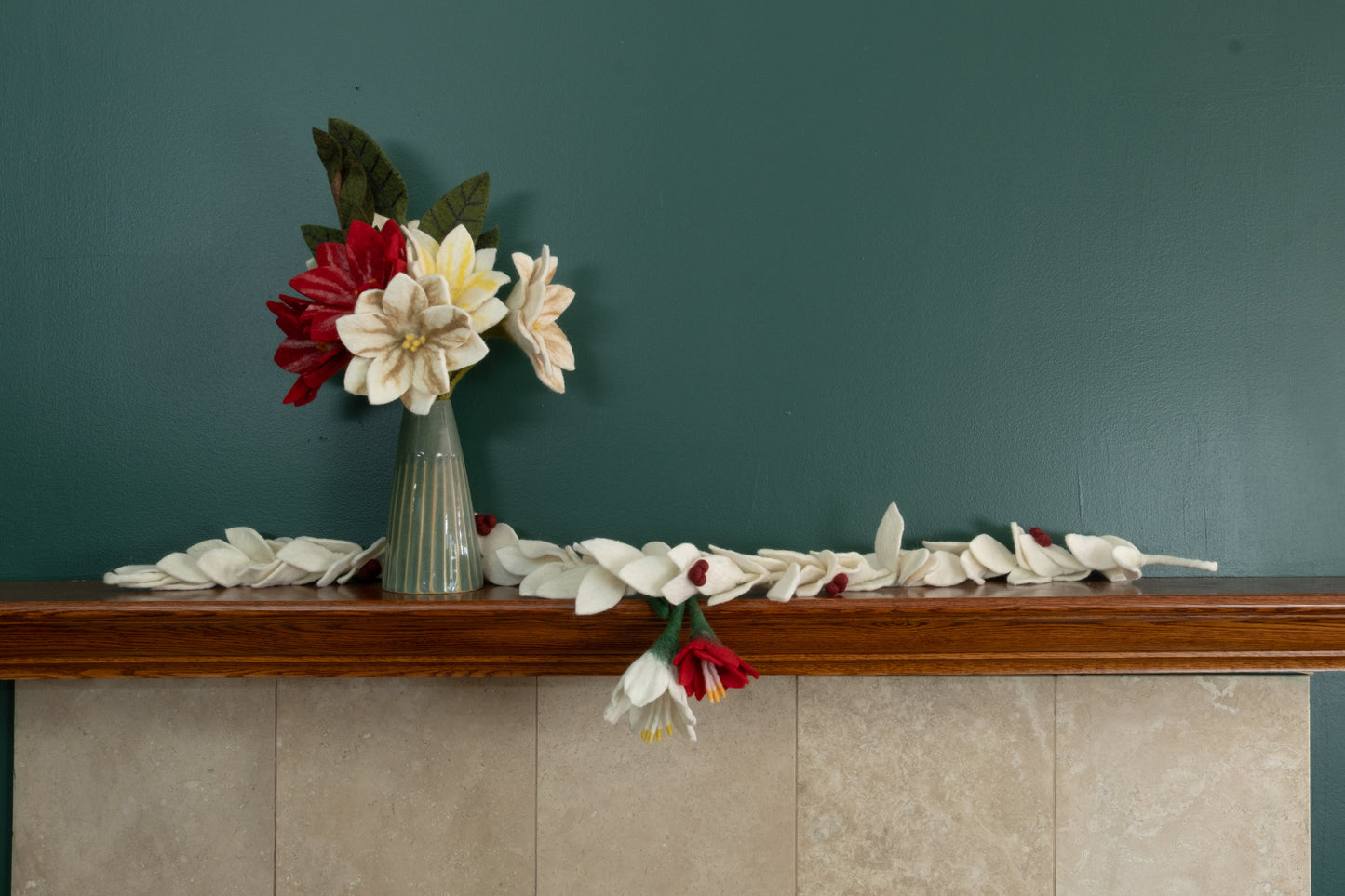 Felt ornaments of a red flower and a white flower hanging from a mantel decorated with Christmas flowers and garlands.