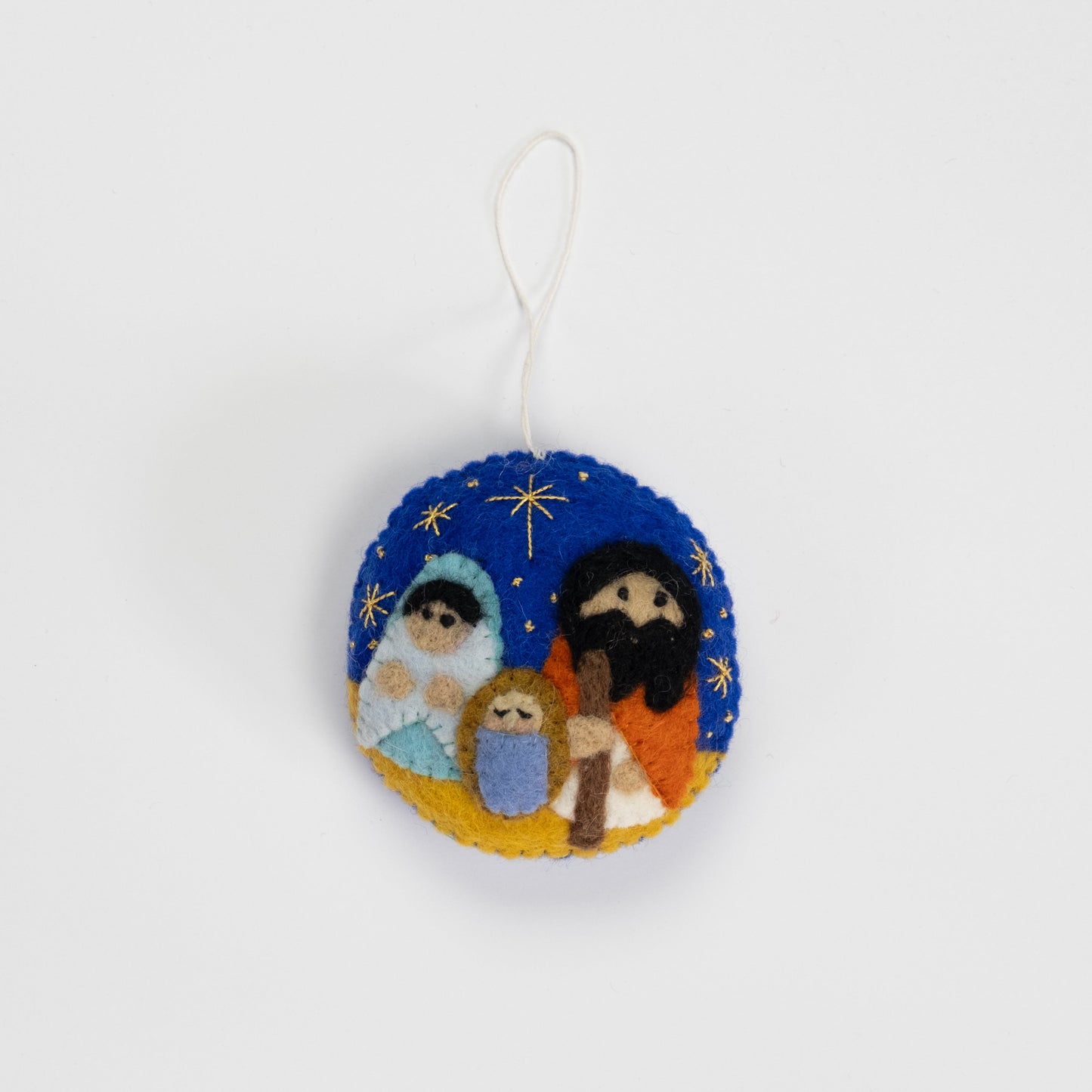 Felt ornament in a circle shape showing the nativity scene of Mary, Joseph, and baby Jesus underneath the night sky.