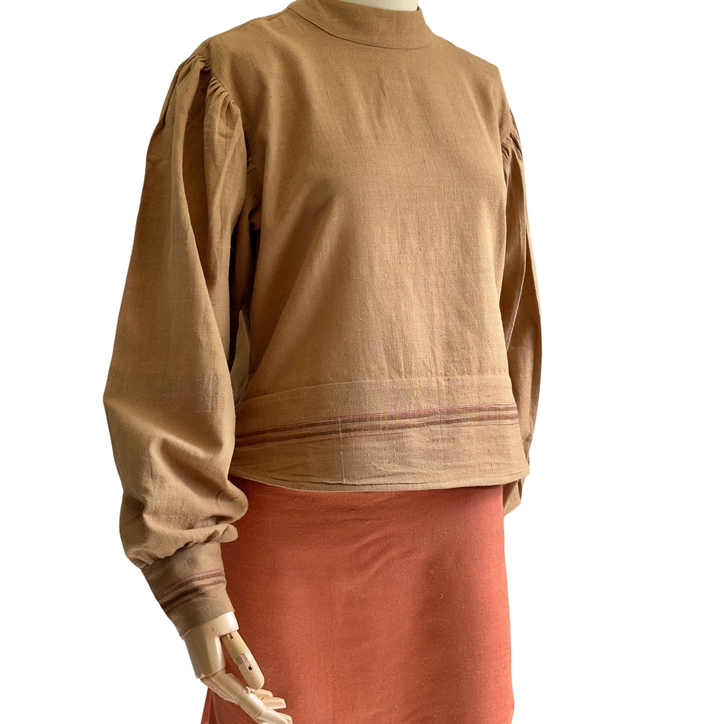 Partial view of manikin wearing brown woven long sleeve shirt and orange skirt.