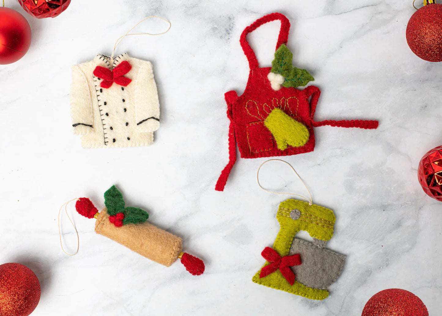 Scattered felt ornaments of a chef's coat, red apron, rolling pin, and green mixer with red bow.