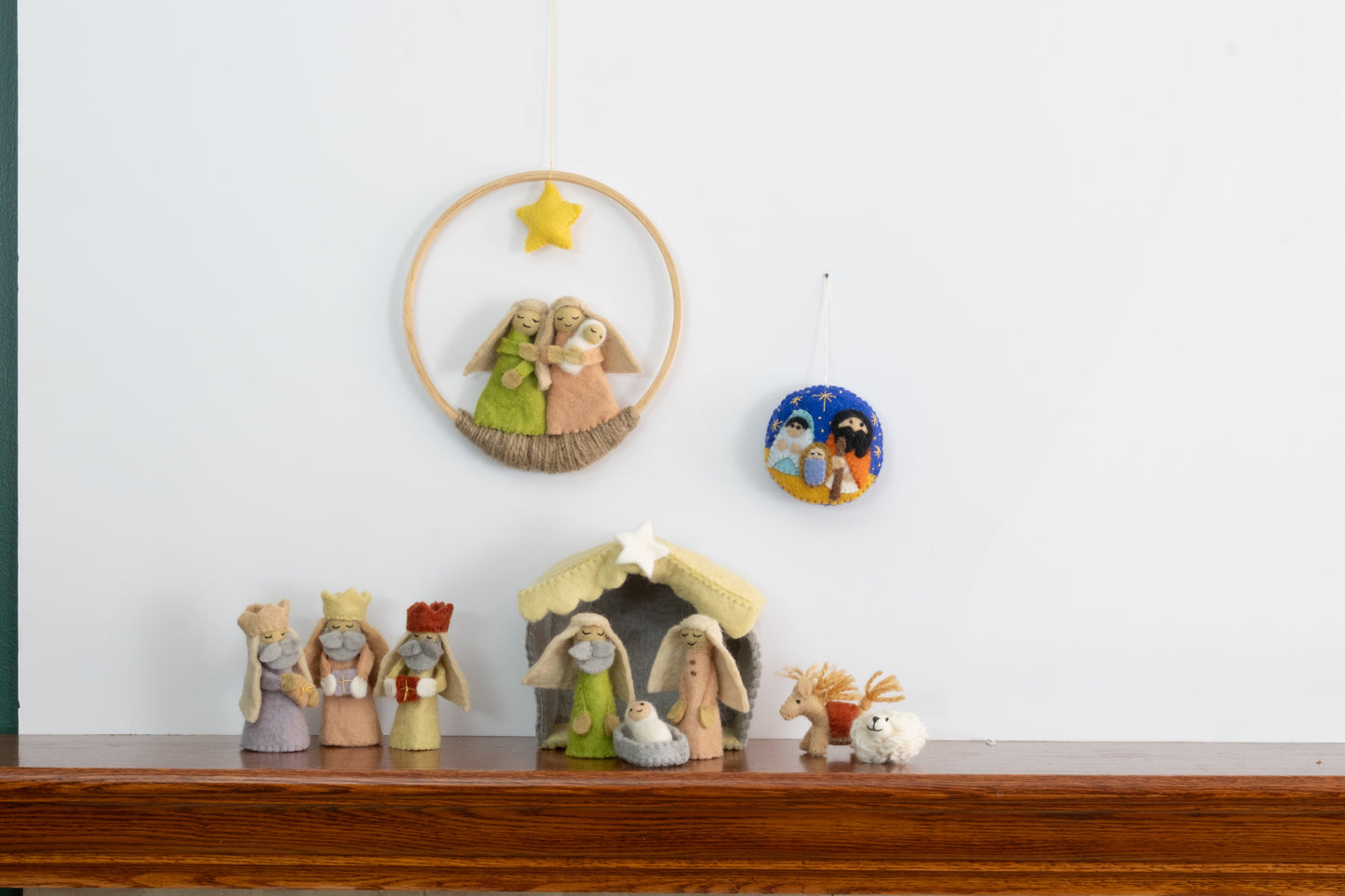 Felt ornament in a circle shape showing the nativity scene of Mary, Joseph, and baby Jesus underneath the night sky behind a full nativity scene set.