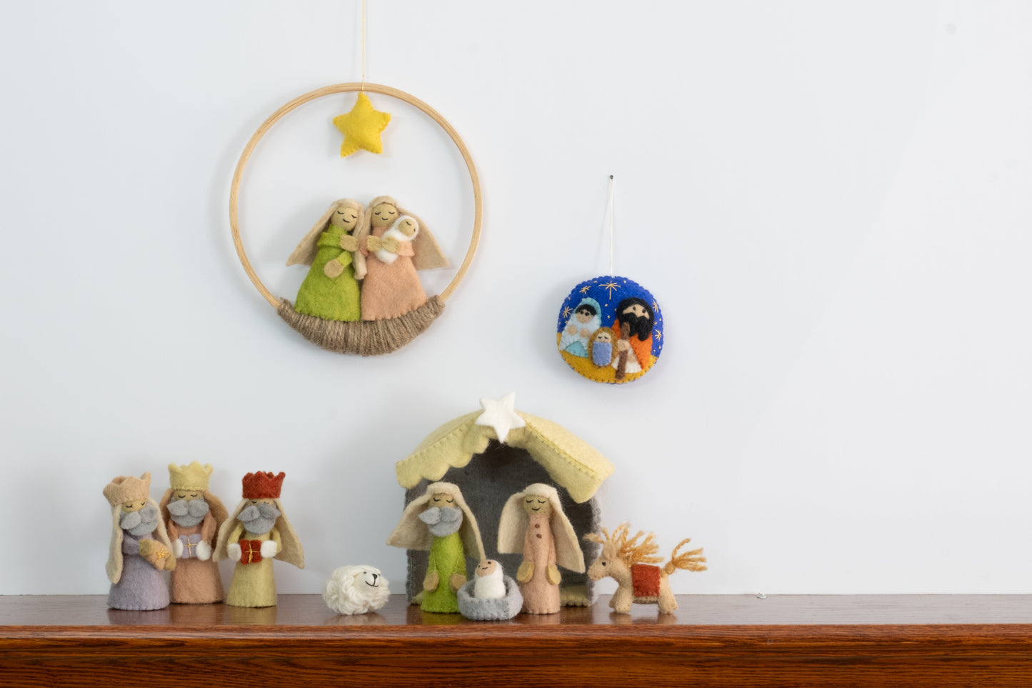Felt ornament in a circle shape showing the nativity scene of Mary, Joseph, and baby Jesus underneath the night sky behind a full nativity scene set.