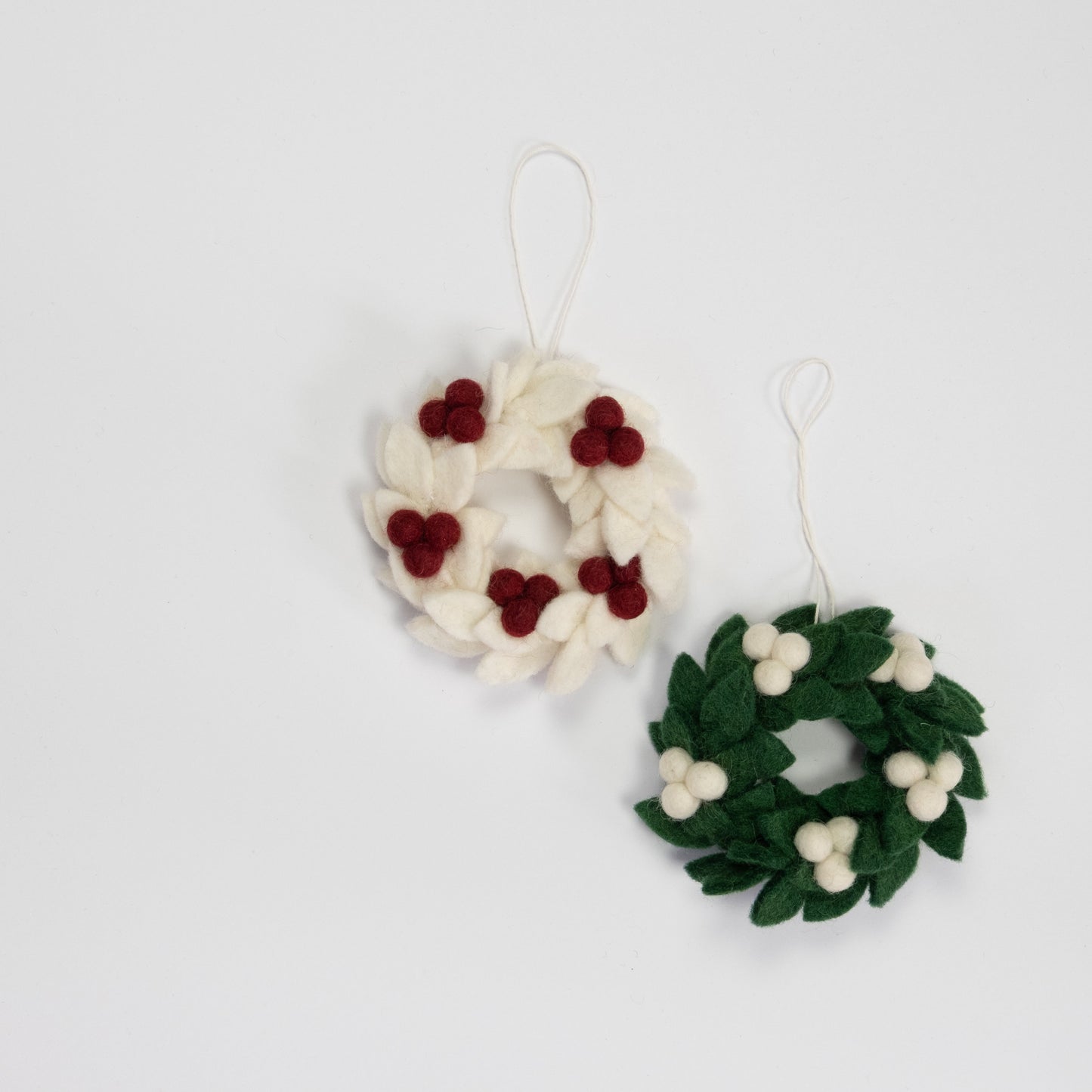 Felt ornaments of mini wreaths, one in white with red berries and the other in green with white berries.