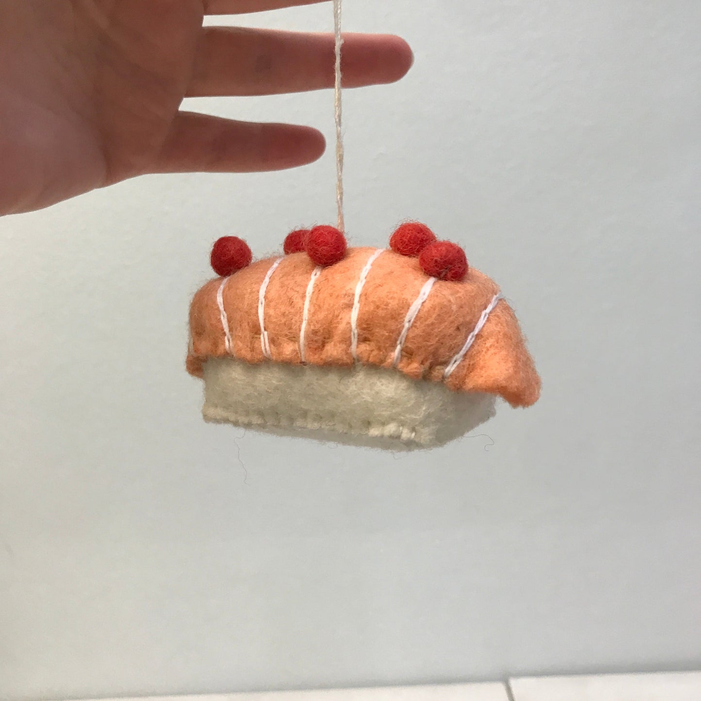 Hand holding a felt ornament of salmon on rice sushi piece.