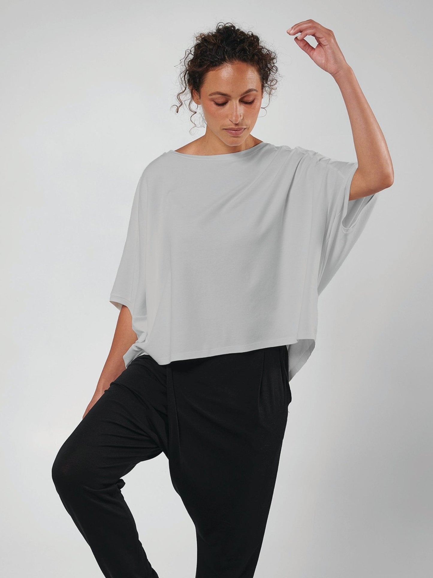 Woman wearing a light gray oversized shirt over a black outfit on a white background.