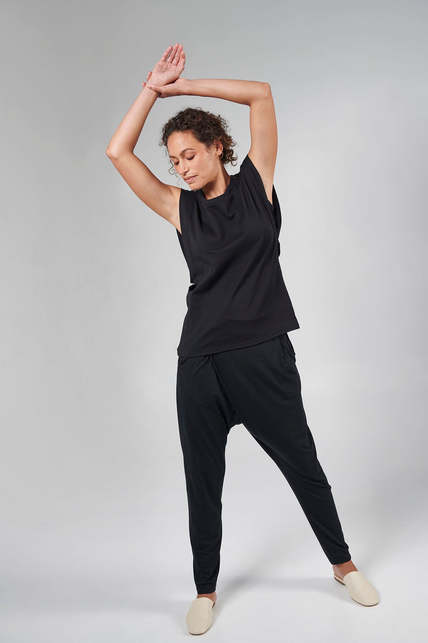 Woman wearing black short sleeve top. Arms are overhead, right foot in front of left foot, wearing white shoes.