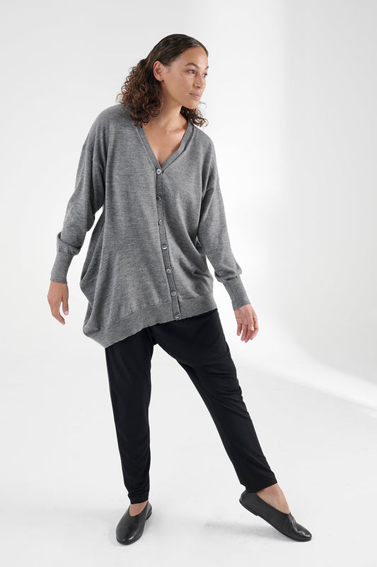 Front view of woman wearing grey cardigan, left foot pointing, body tilted to the left.