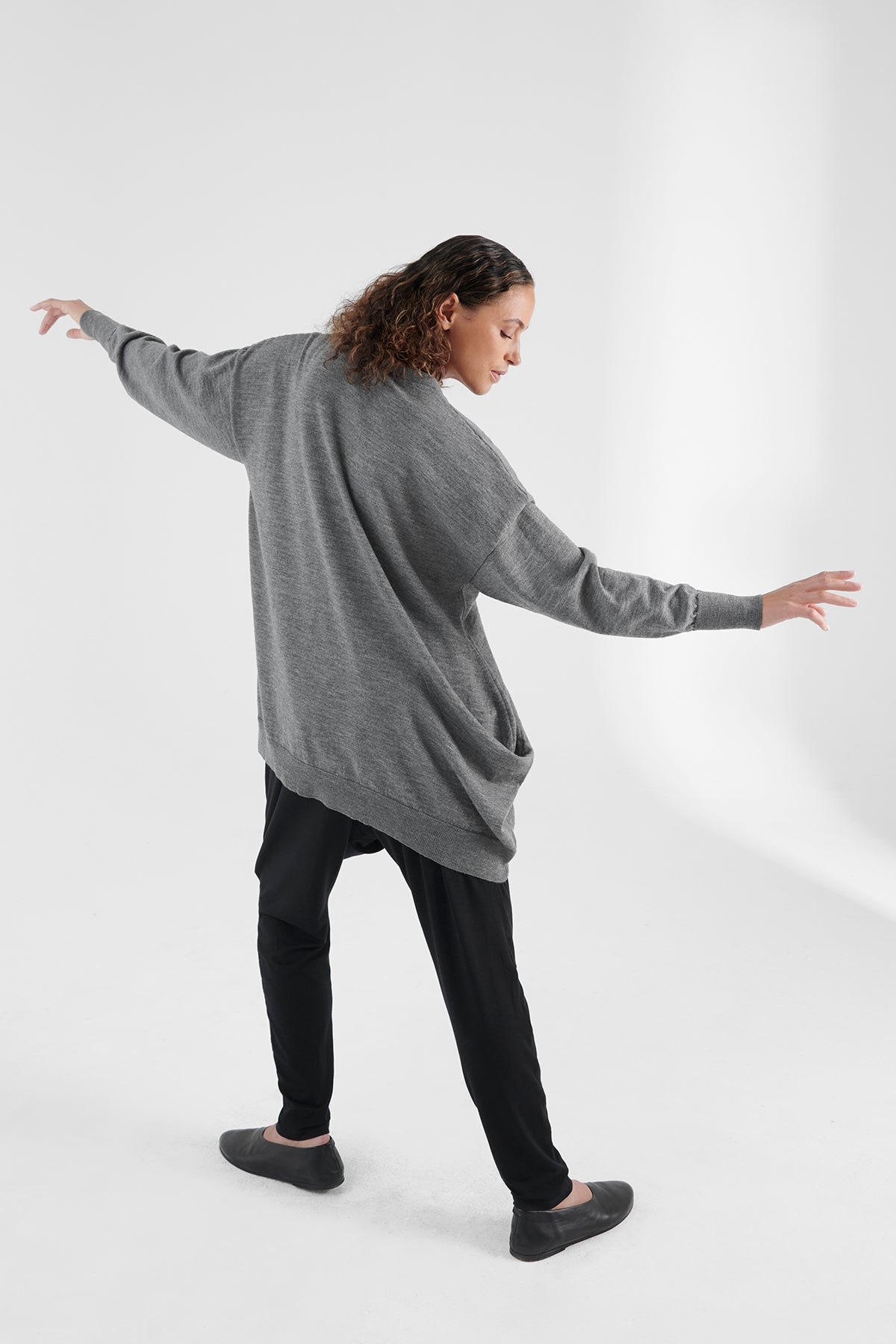 Back view of woman wearing grey cardigan, arms spread out.