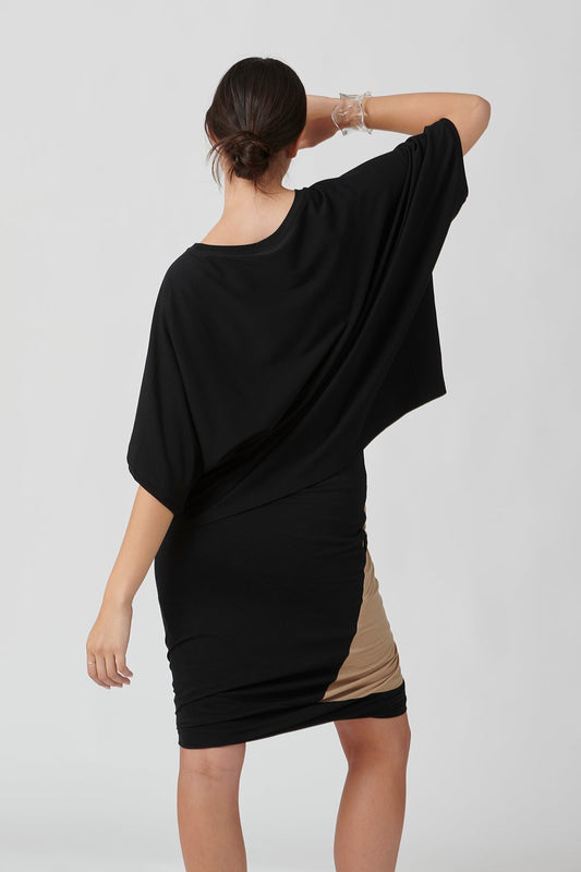 Back view of woman wearing black top and tan with black accent skirt, right hand on forehead.