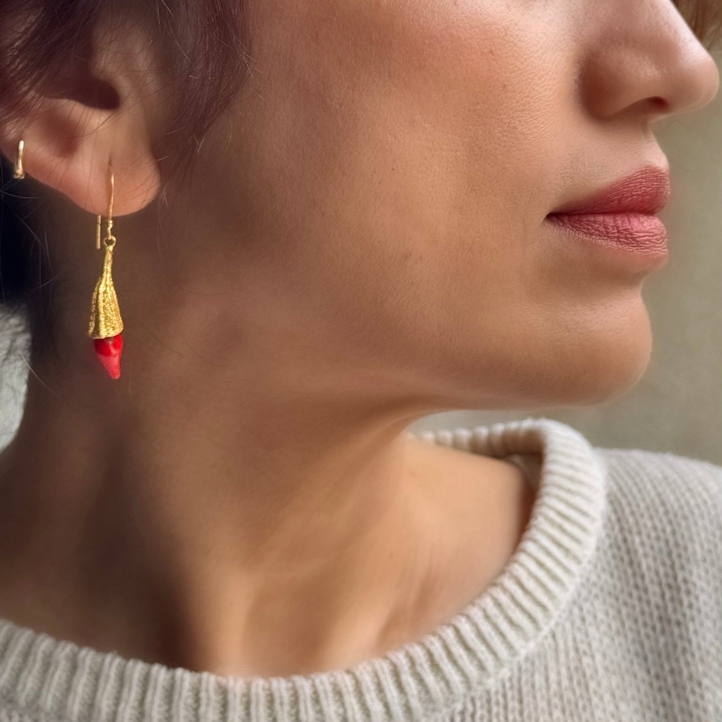 Right side view of woman wearing red chili pod and gold hanging earrings.