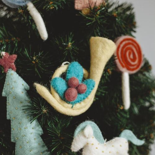 Felt ornament of a French Horn with a sprig of holly and berries on a Christmas tree.
