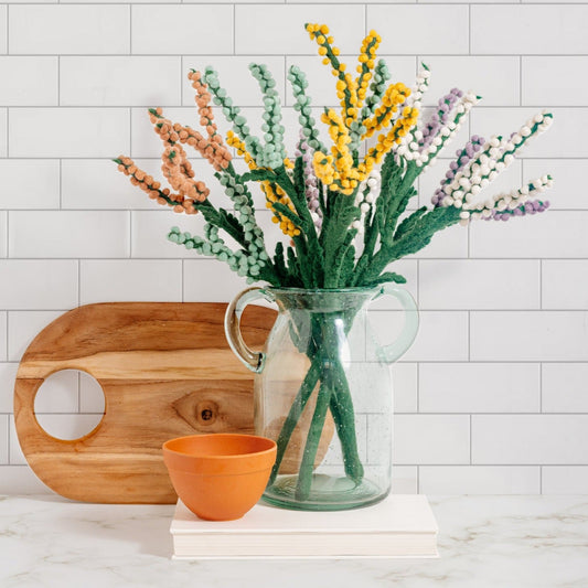 Bouquet of felt Baby's Breath flowers in peach, yellow, purple, white, and blue in glass vase on countertop.