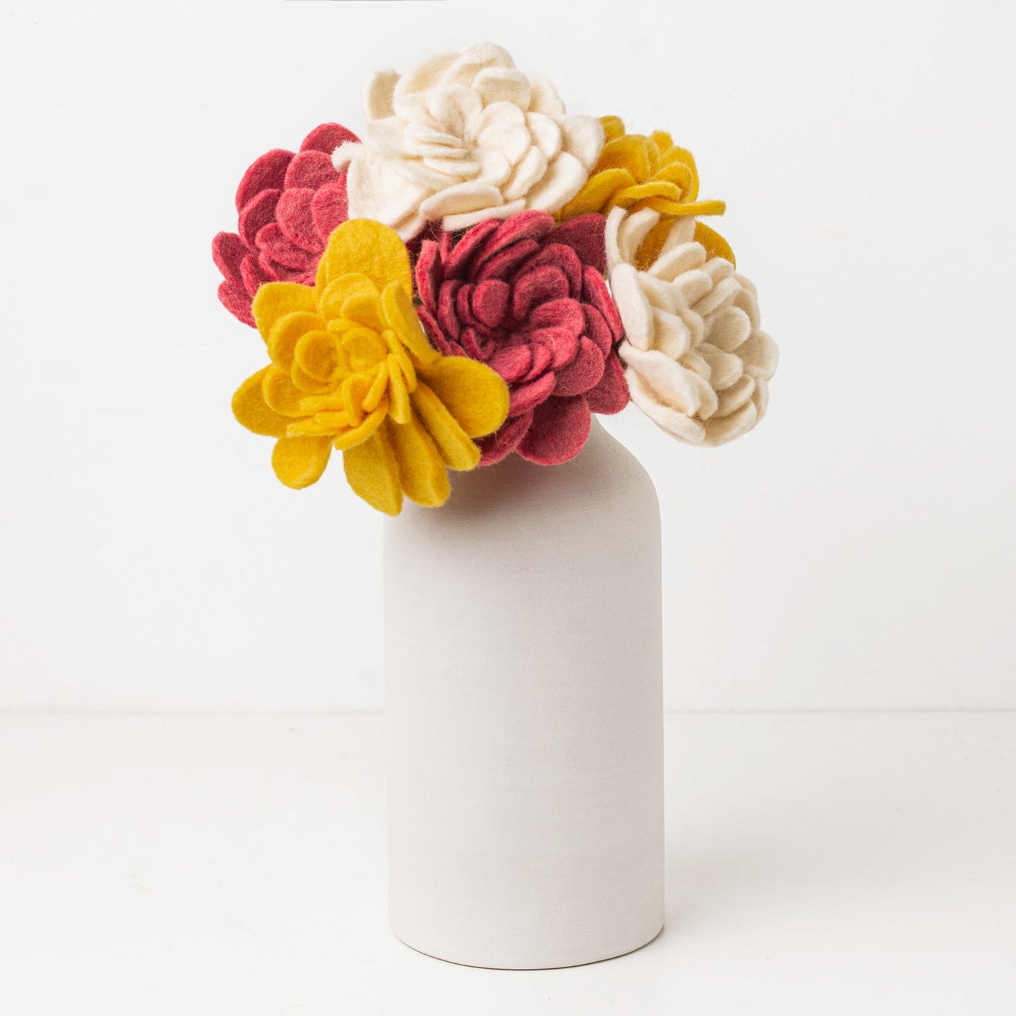 Yellow, pink, and white felt floral arrangement in a white vase.