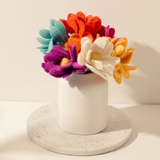 Bunch of felt daisies in yellow, orange, reddish orange, bright pink, light blue, purple, and white in a white vase.