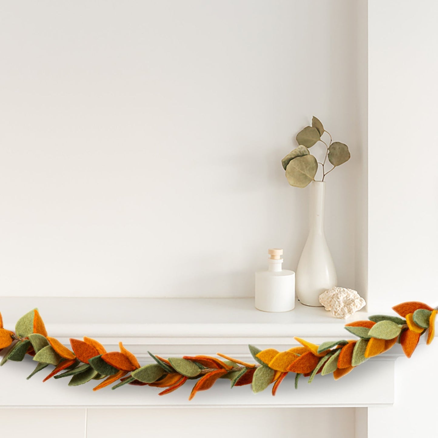 Felt garland of leaves in orange and green hanging from white mantel.