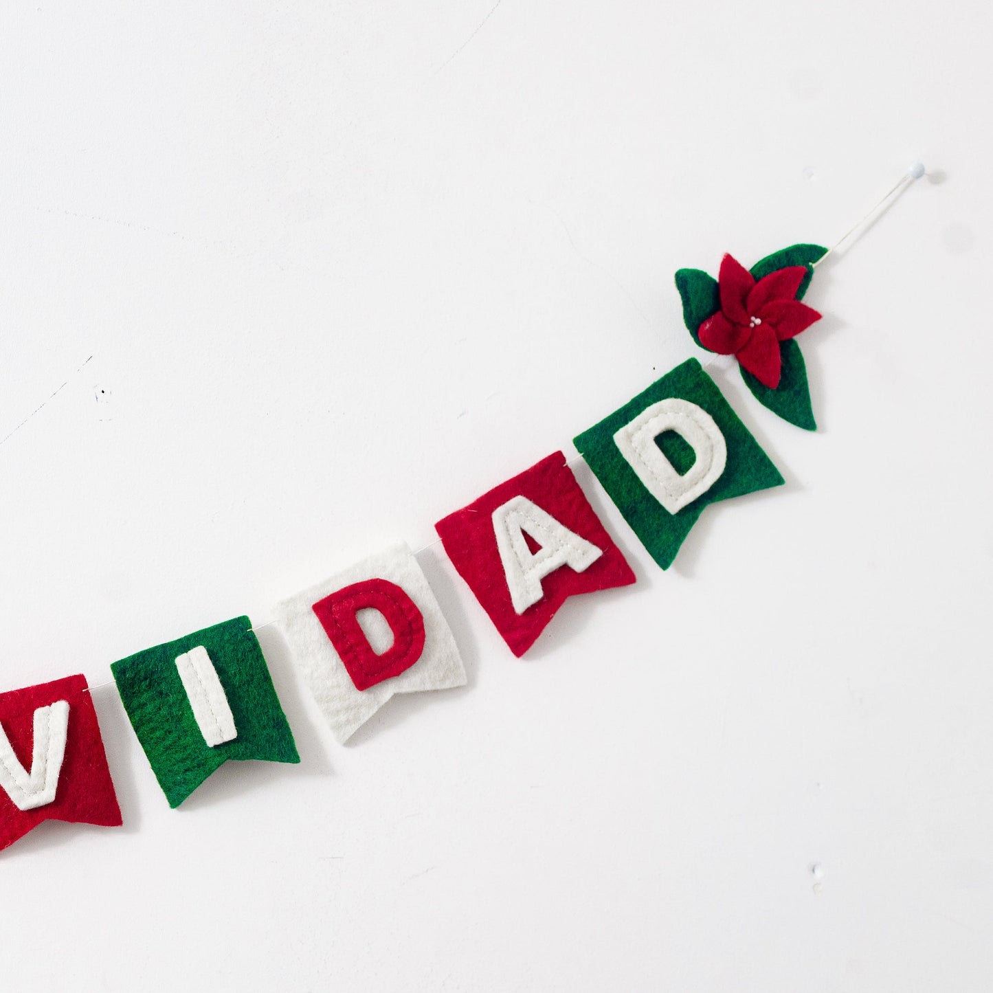 Close up of felt garland spelling out Feliz Navidad in red and white letters on small dovetail flags in white, red, and green.