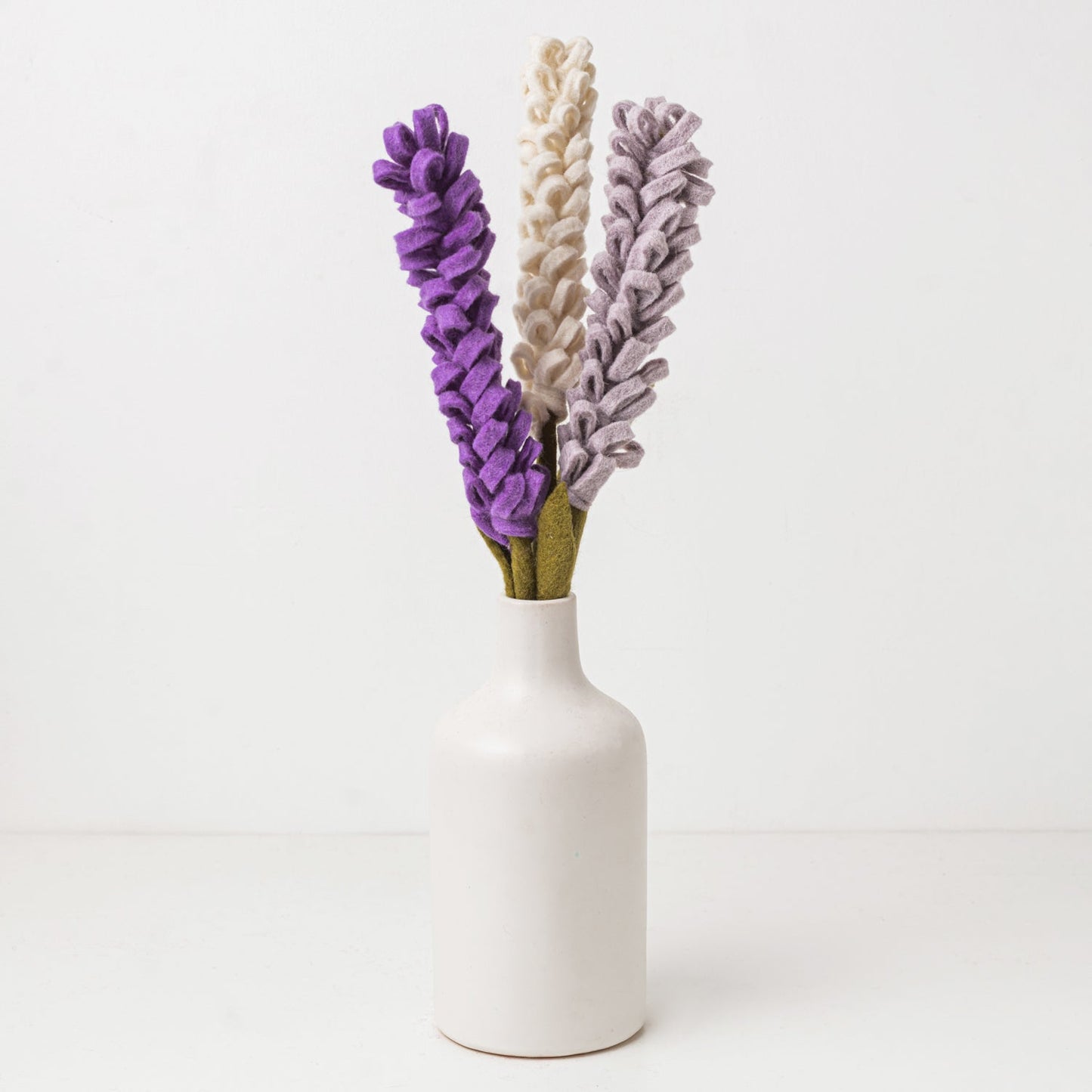 Purple and white felt floral arrangement in a white vase.