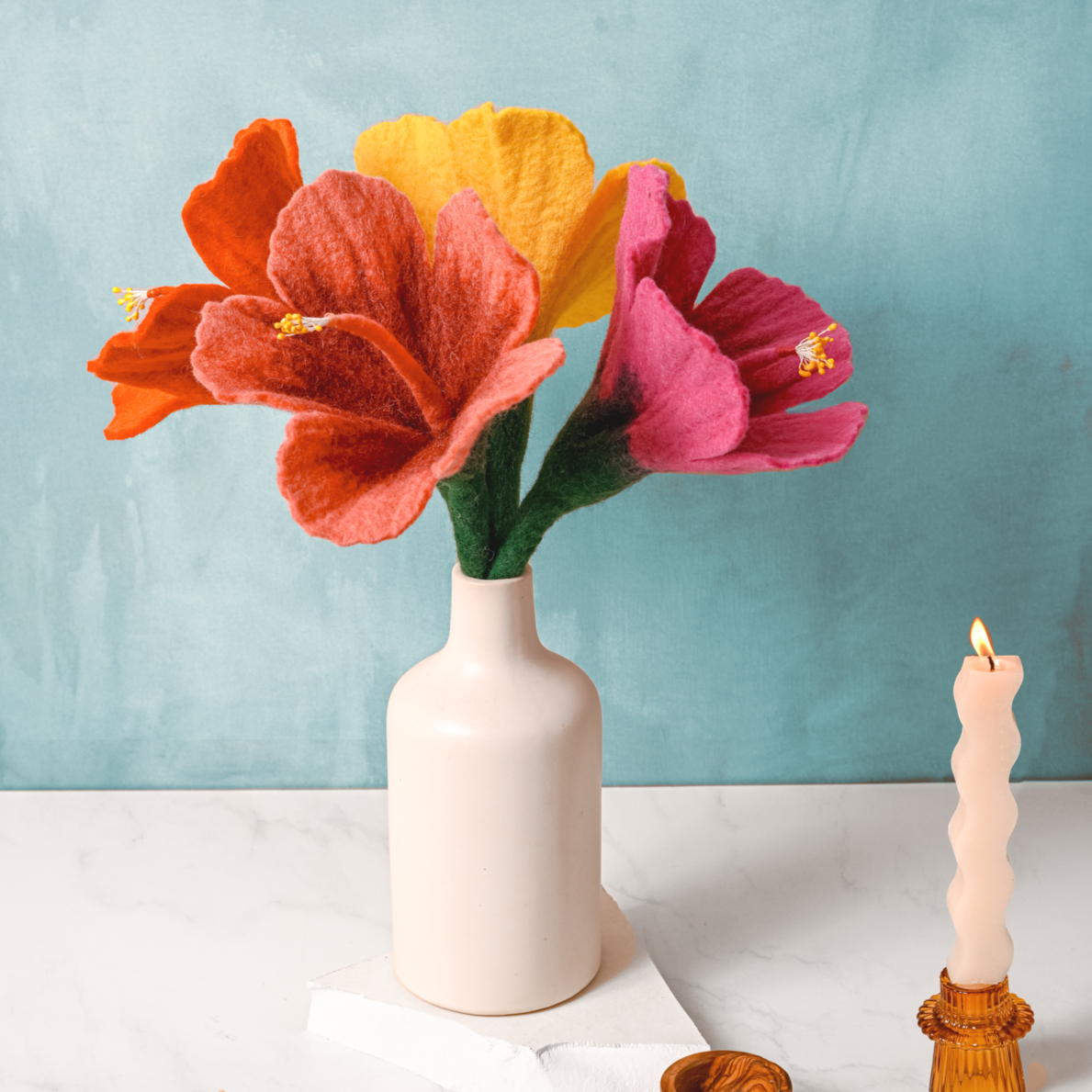 Coral pink, red, yellow, and bright pink felt hibiscus flowers in a white vase.