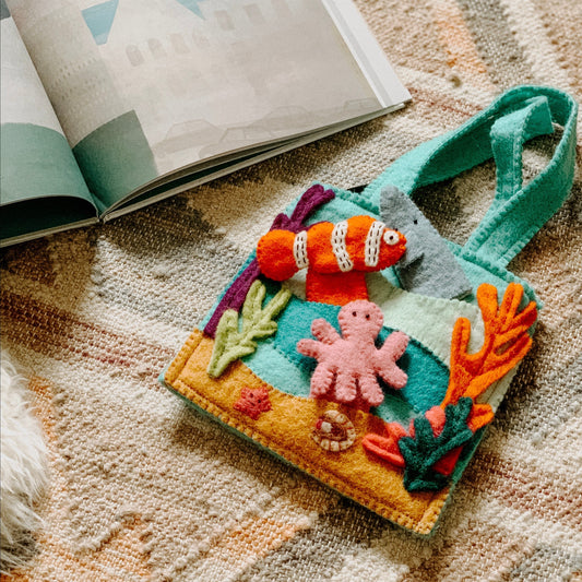 Felt bag on a rug with under the sea finger puppets of an orange and white clown fish, a pink octopus, and a grey shark.