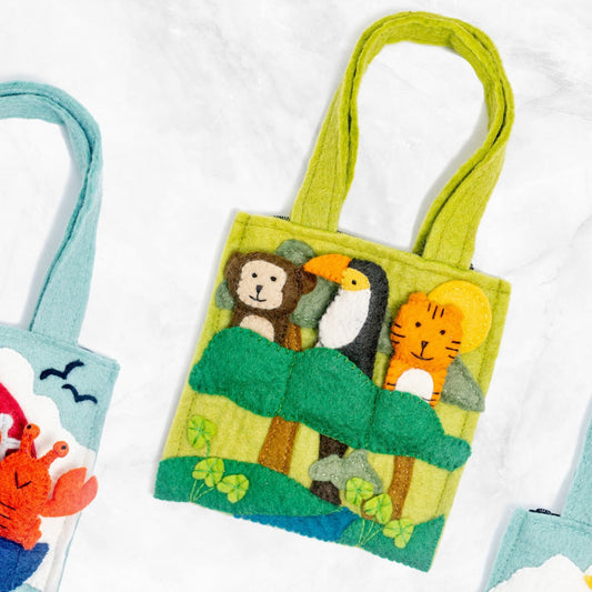 Green felt puppet bag with a monkey, toucan, and tiger finger puppets in trees laying next to other puppet bags.