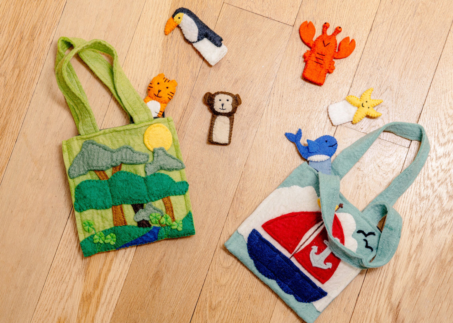 Green felt puppet bag with a monkey, toucan, and tiger finger puppets in trees laying next to a sail boat puppet bag.