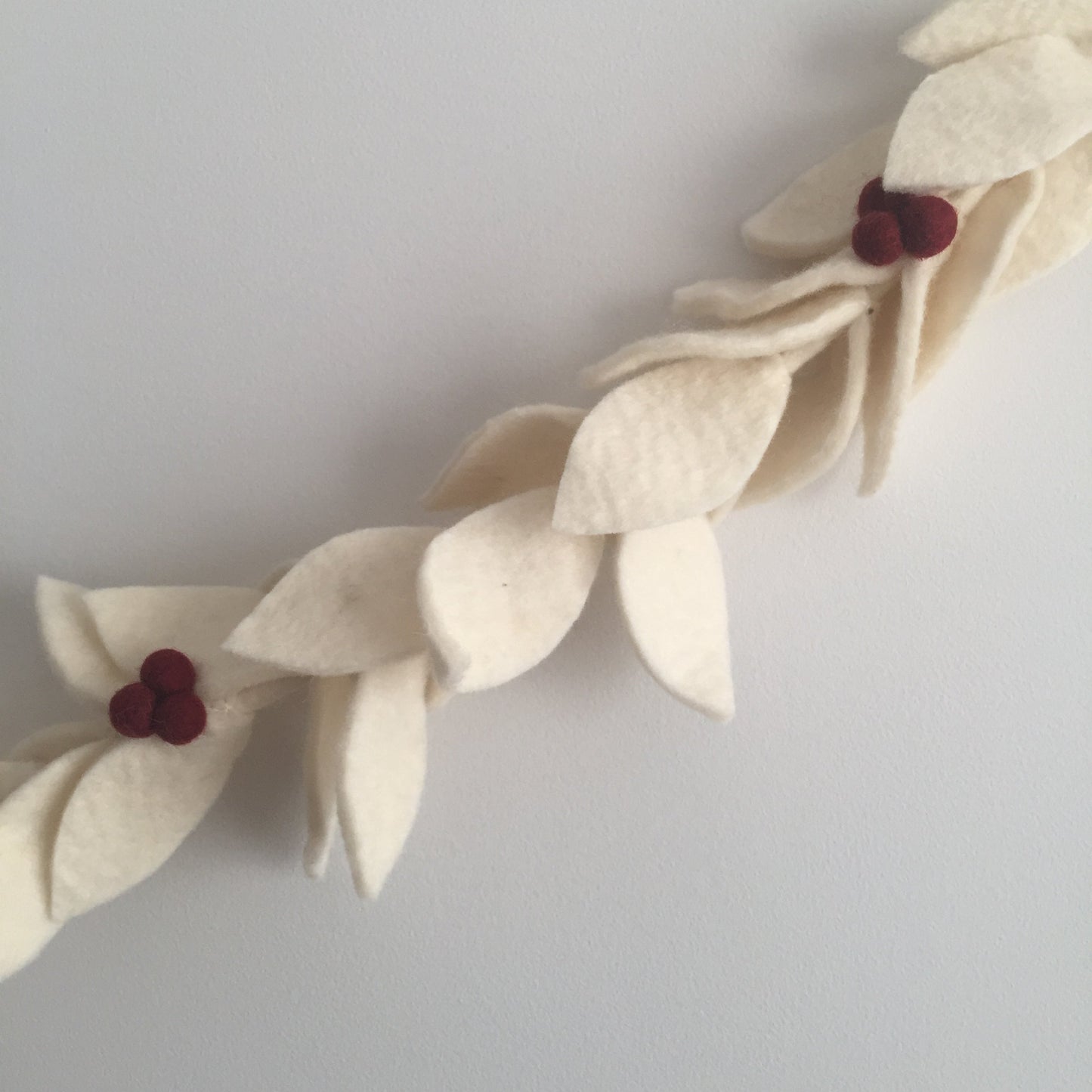 Felt garland with white leaves with red berries hanging on wall.