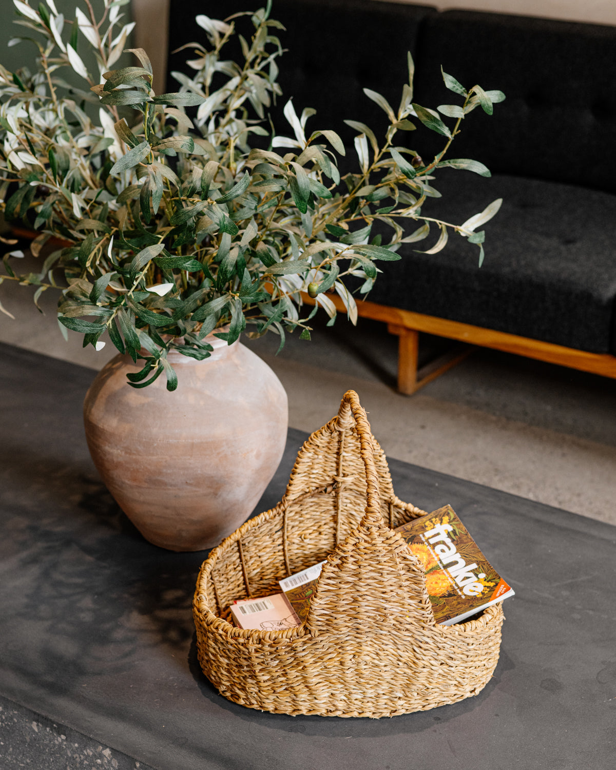 Brown woven magazine basket with handle on floor next to plant.