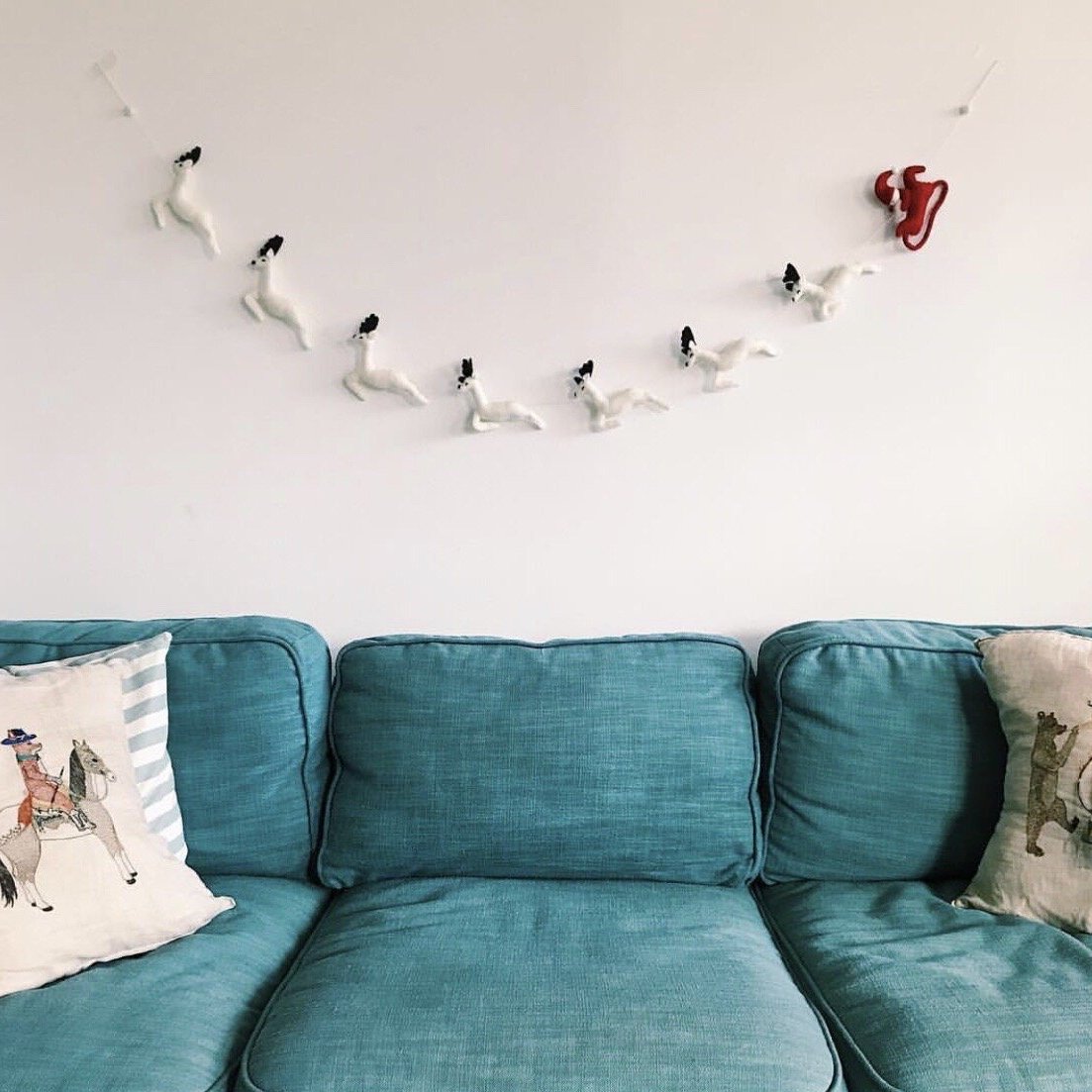 Felt garland red Santa and sleigh with white reindeer hung over blue couch.