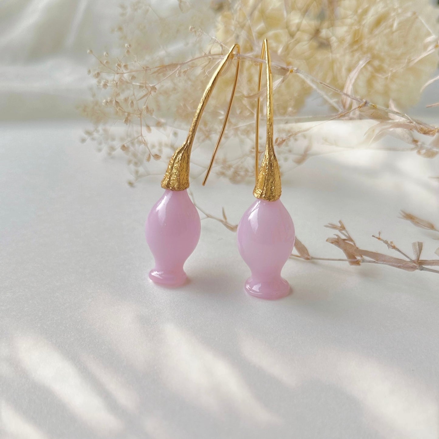 Pair of pink glass earrings with gold plated findings. Dried flowers in upper area of image.