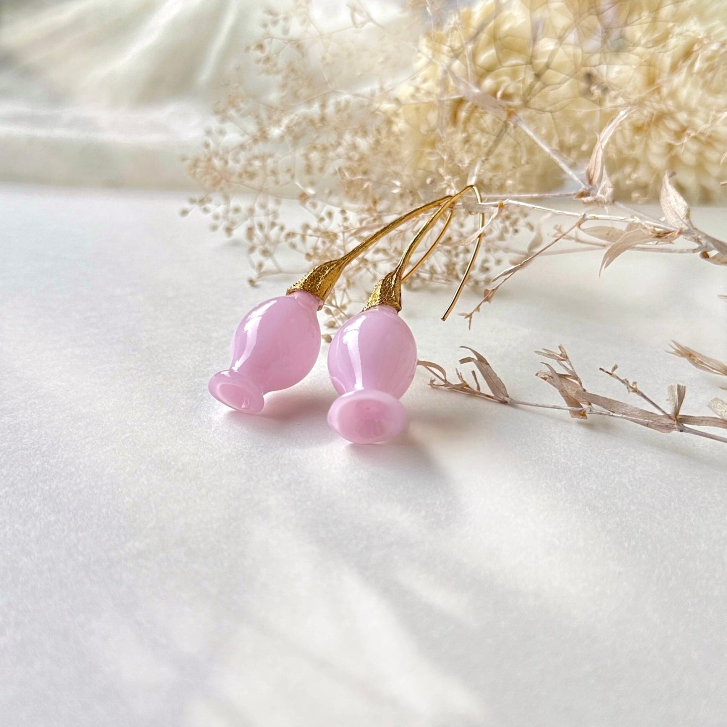 Pair of pink glass earrings with gold plated findings. Dried flowers in upper area of image.