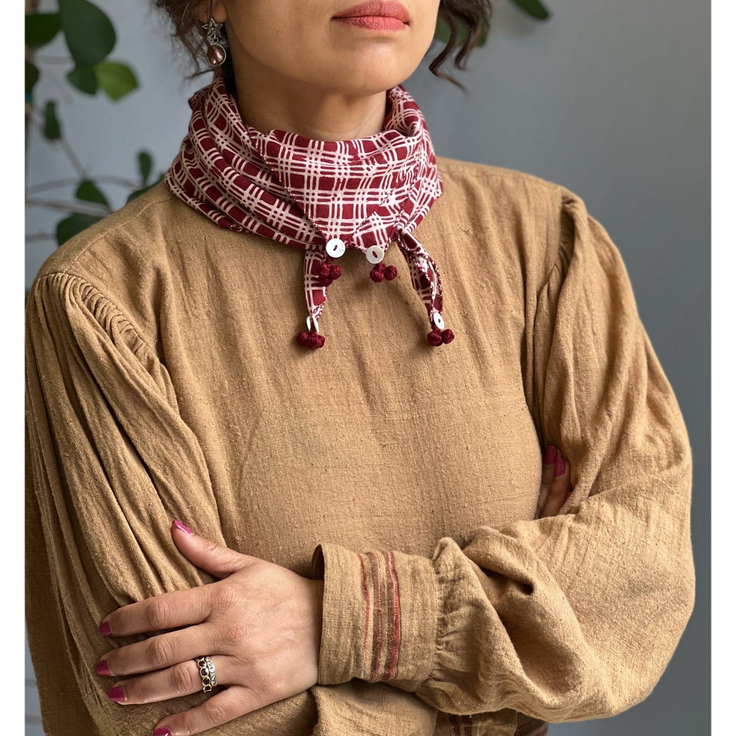 Partial view of woman wearing brown woven long sleeve shirt with red and white bandana, arms crossed in front.