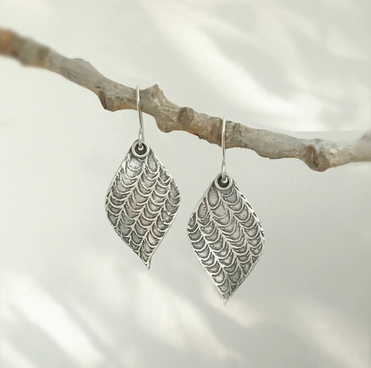 Pair of silver leaf earrings hanging from branch.