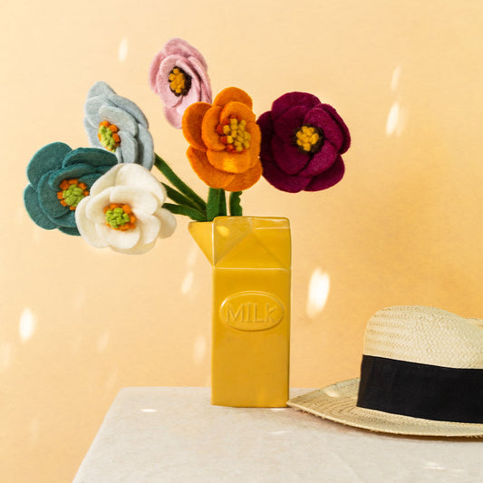Bouquet of felt poppy flowers in magenta, blue, pink, white, orange, and light blue in a yellow vase.