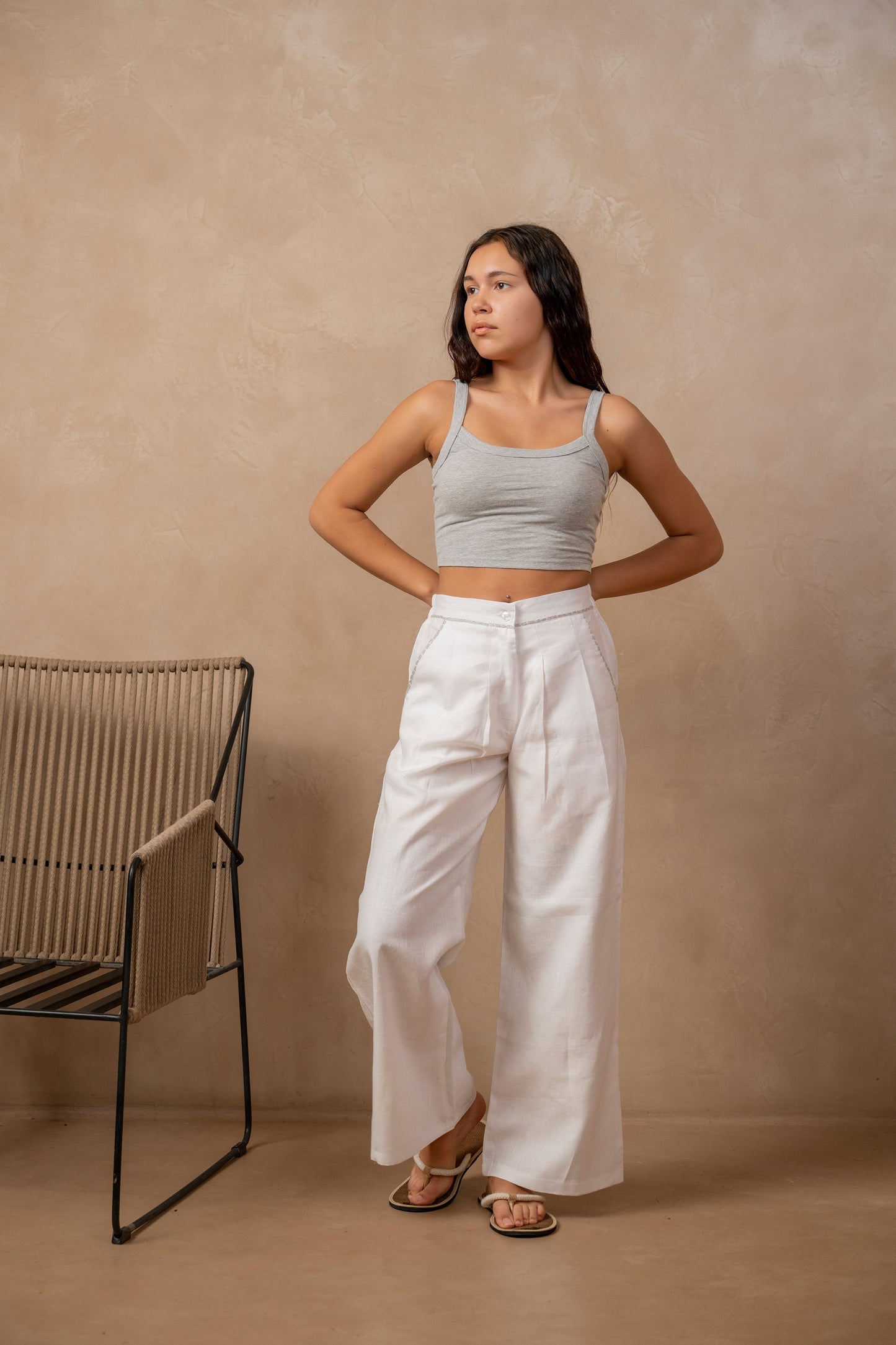 Front view of woman wearing white Dhara Pleated Wide Leg Pants and crop top, right leg bent, hands behind back.