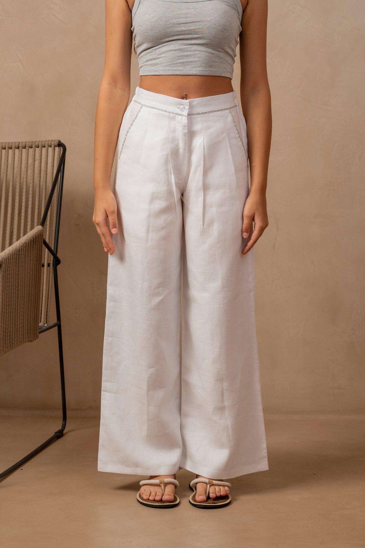 Partial front view of woman wearing white Dhara Pleated Wide Leg Pants and a crop top, hands at her side.