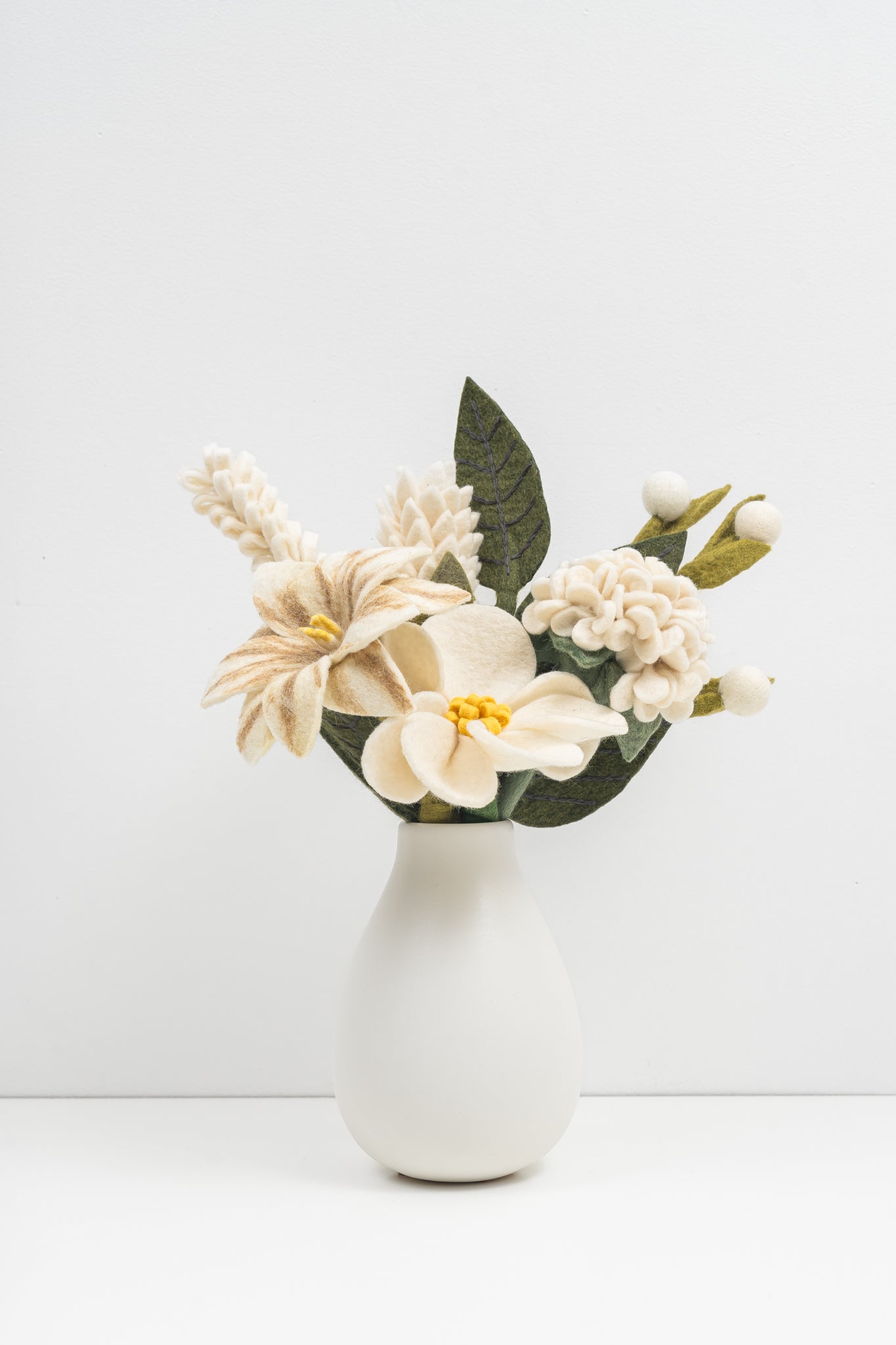 White vase with a bouquet of crisp white felt flowers on a white background. Handmade in Nepal by artisans earning a fair wage.