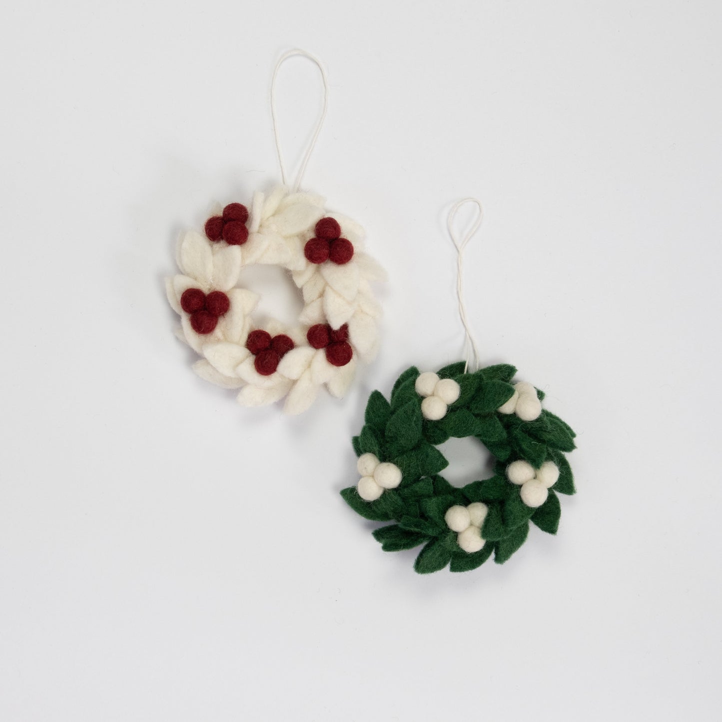 Felt ornaments of mini wreaths, one in white with red berries and the other in green with white berries.