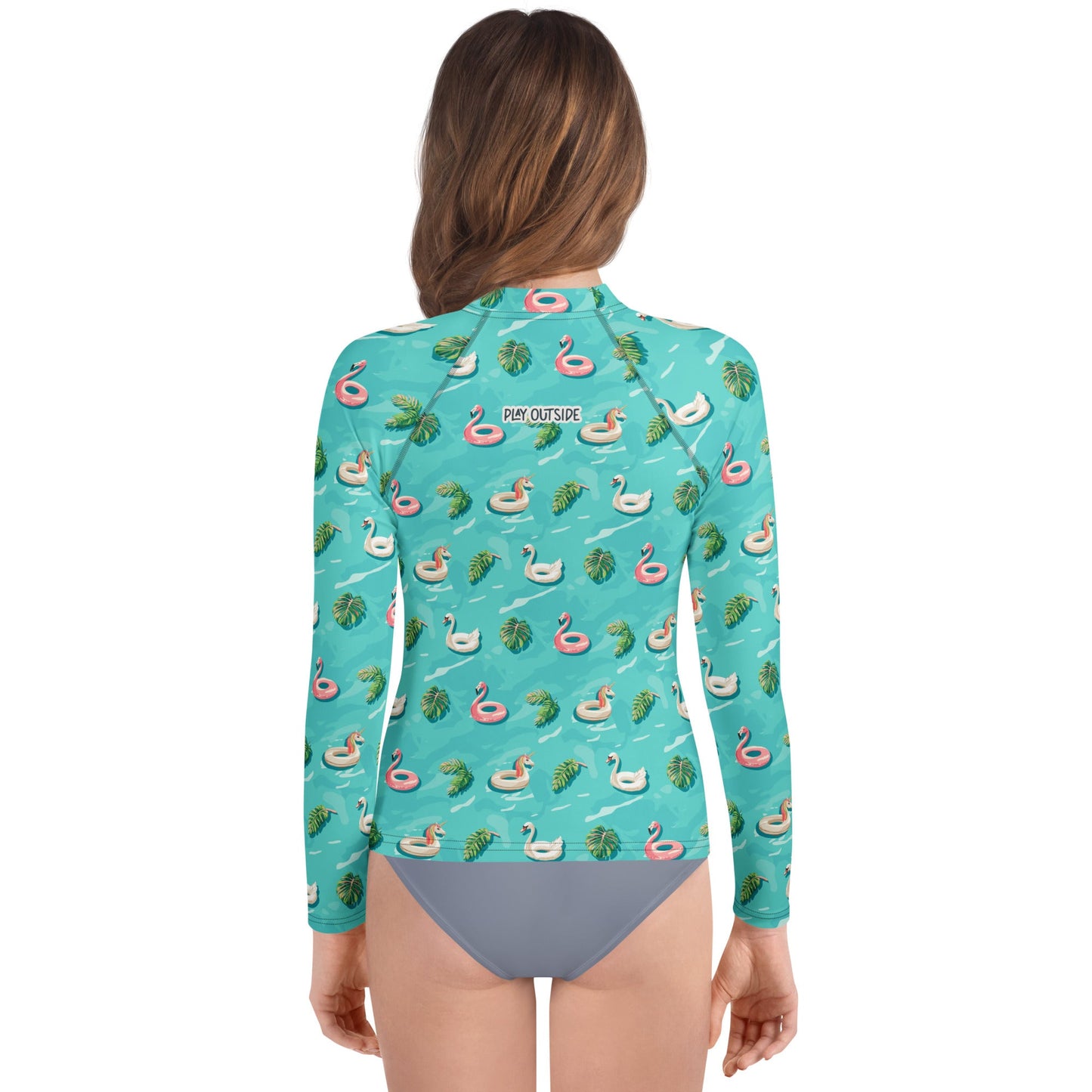 Back view of girl wearing an aqua blue rash guard with images of pink floaty toy unicorns, swans, and Flamingos and green tropical leaves.