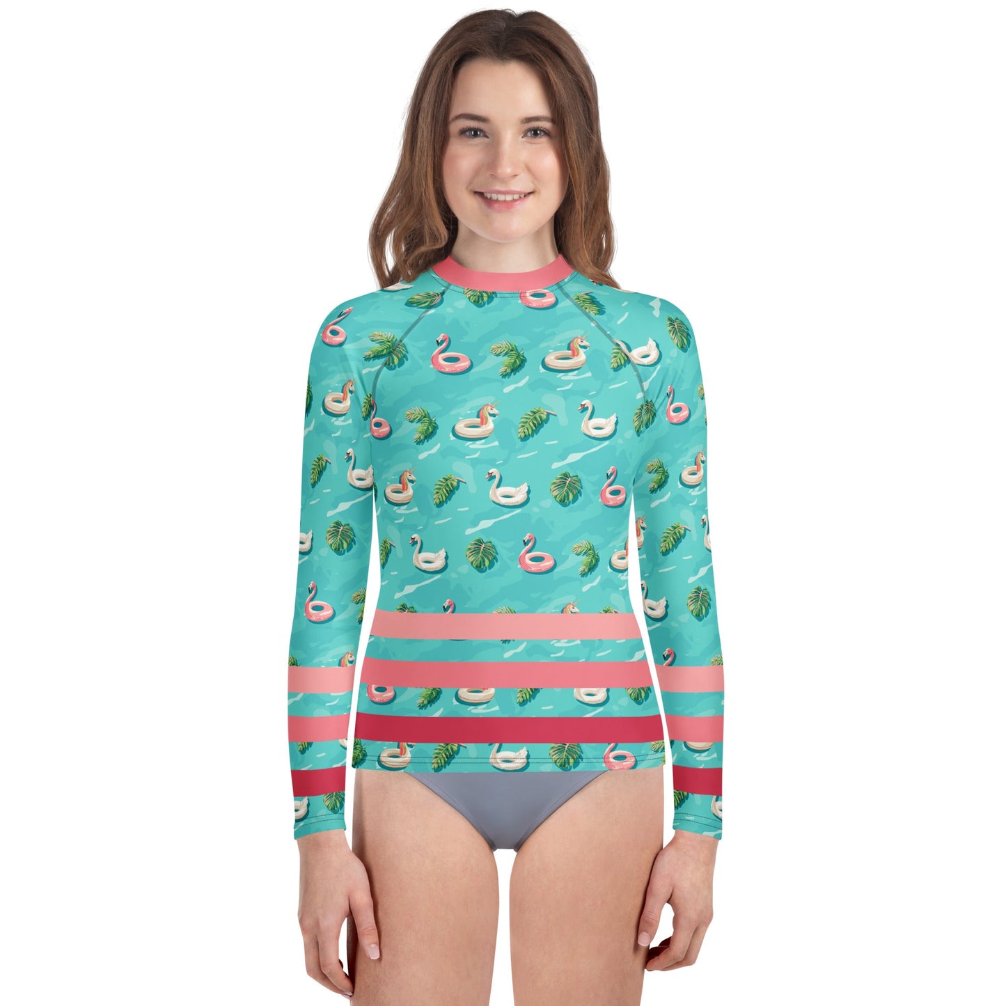 Girl wearing aqua blue rash guard with pink neckline and pink stripes on the lower half and images of pink floaty toy unicorns, swans, and Flamingos and green tropical leaves.