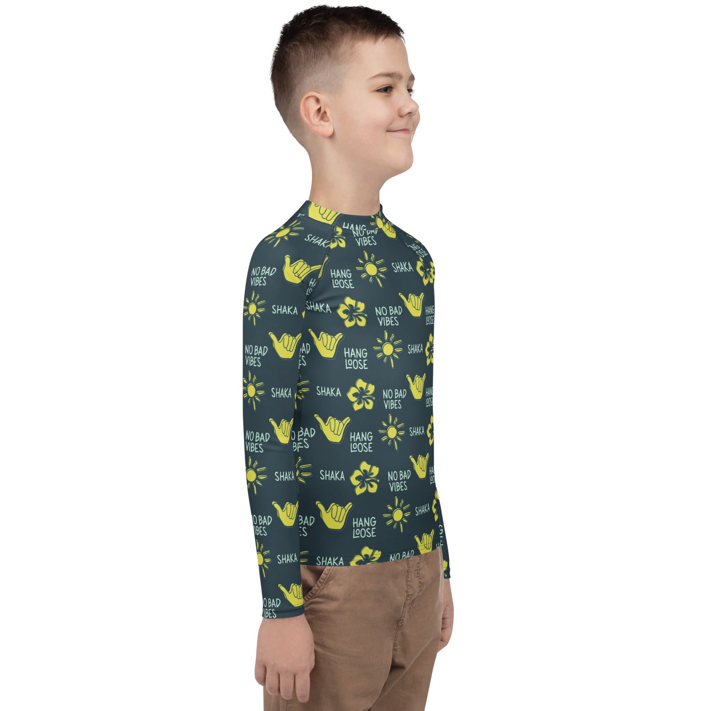 Side view of boy in dark blue rash guard with yellow designs of the sun, hibiscus flowers, hang loose hand sign, and the words hang loose, no bad vibes, and shaka.