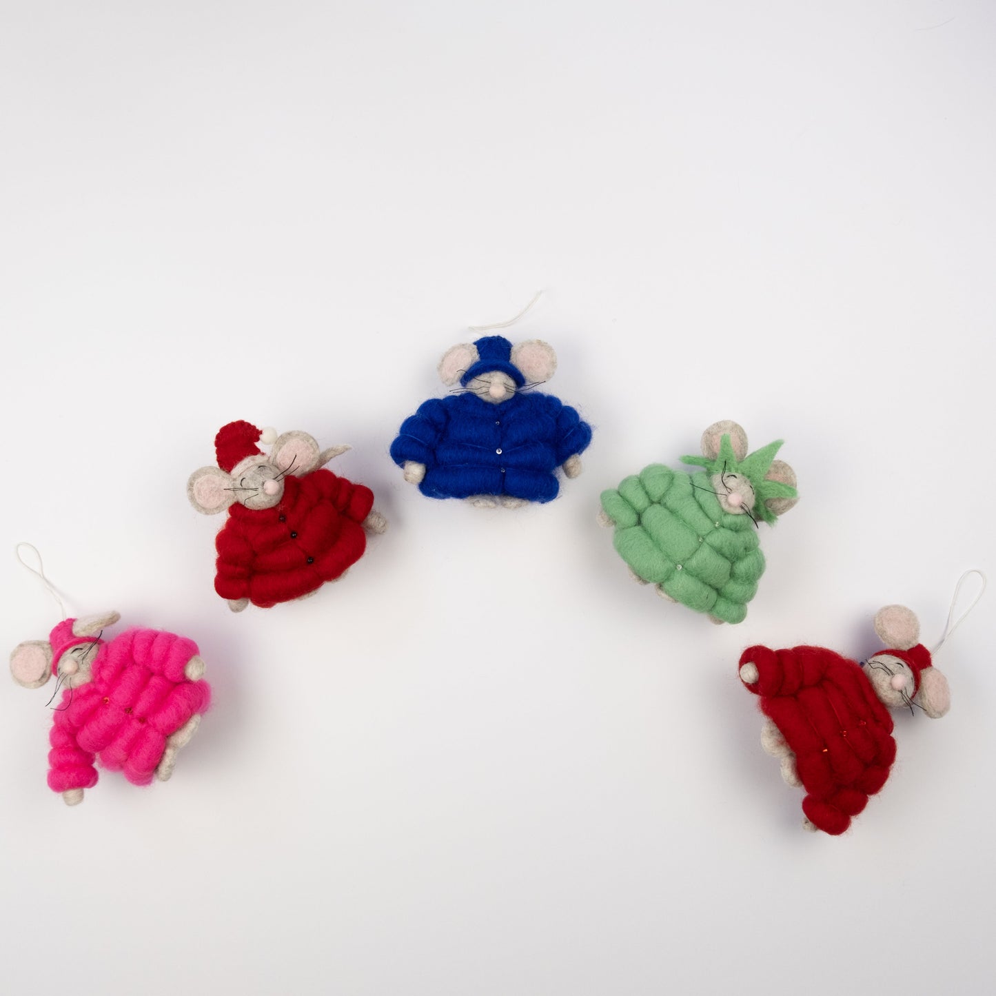 Felt ornaments of mice in pink, red, blue, green and red puffer jackets and various hats or crowns laying in an arc shape.