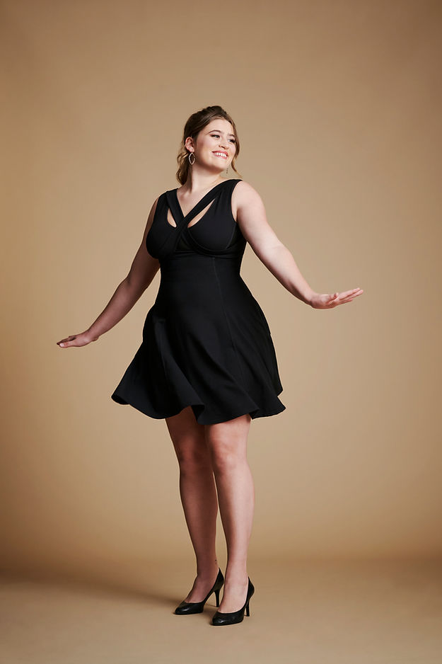 Woman wearing black flare dress with v neck, posed with hands out from sides..
