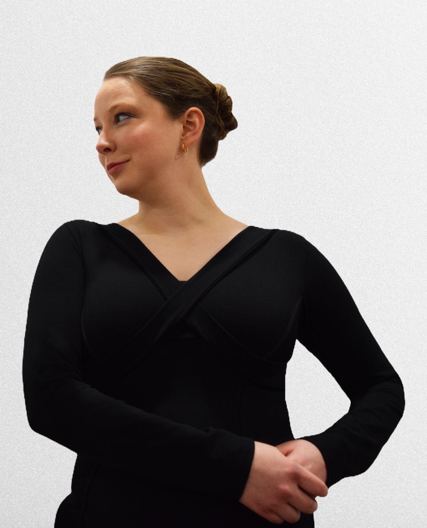Woman wearing black long sleeve v-neck shirt, holding hands at left hip, looking towards right.